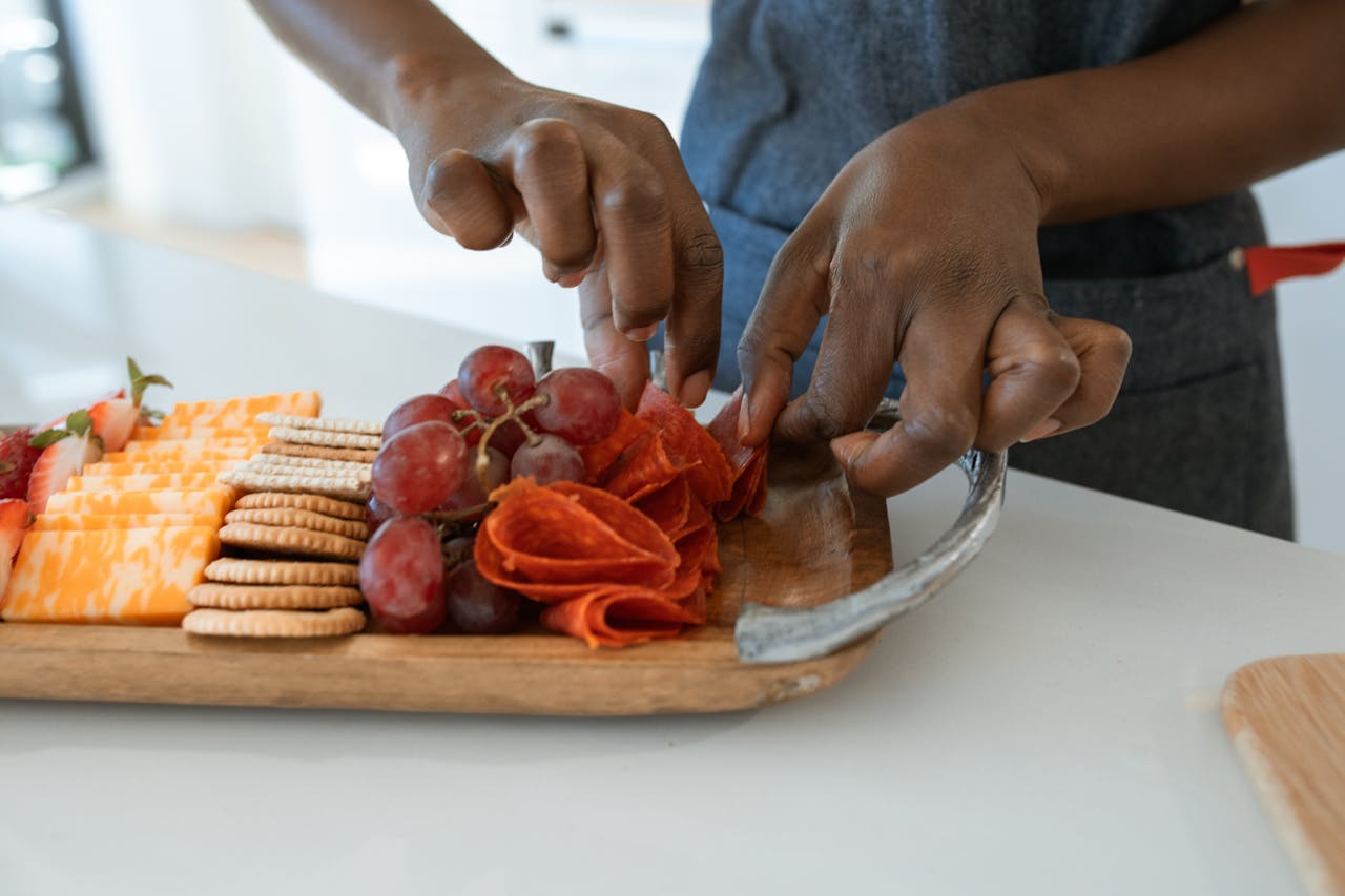 Close-up of hands arranging gourmet charcuterie board with cheese, grapes, and crackers.